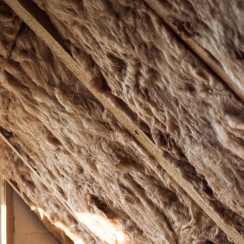 Glass wool and styrofoam in a wooden frame on a inclined wall near the wooden ceiling and a window in a private house. Warming the walls with fiberglass and foam plastic.